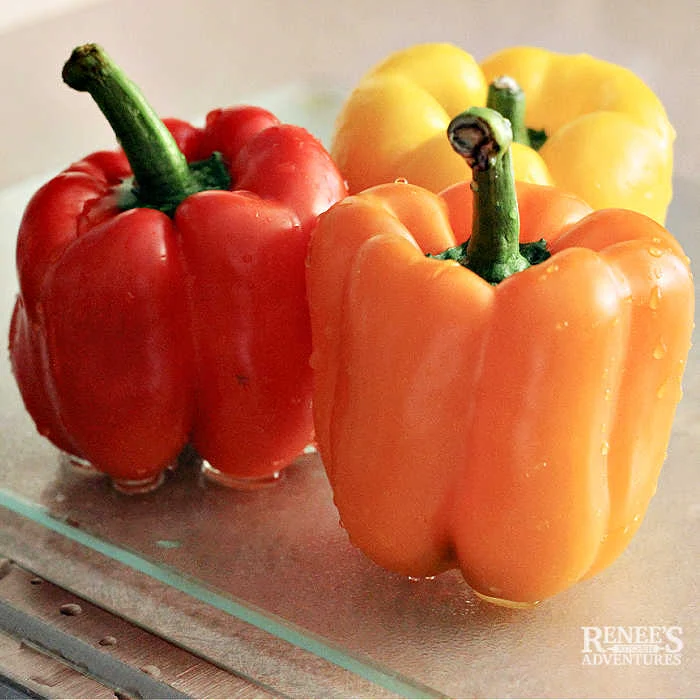 Three washed whole bell peppers red, yellow, and orange color