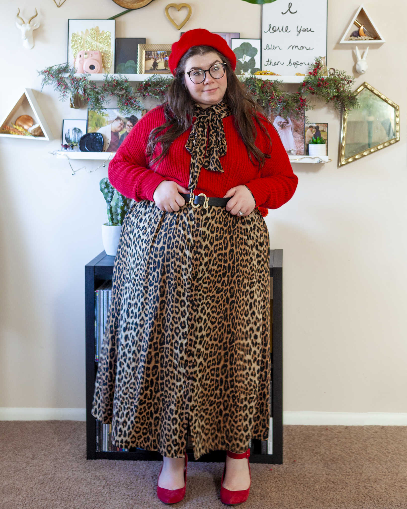 An outfit consisting of a red beret, red crewneck cropped sweater over a leopard print maxi shirt dress and red suede slingback heels.