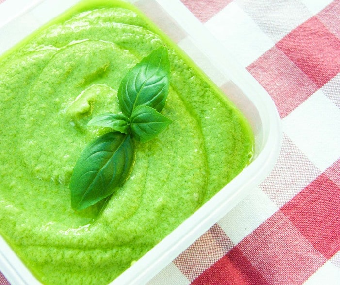 a tub of pea pesto topped with a sprig of fresh basil