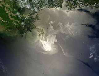 Satellite image of green coastline and dark blue water, with a large gold oil slick visible in the middle of the frame.