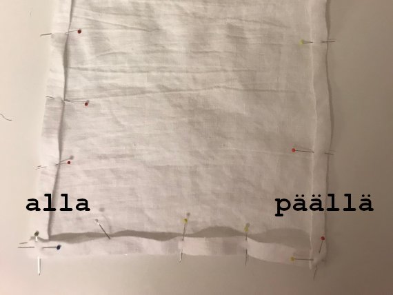 Aluslakanan kulmien asettuminen ja ompelu. Kuvassa on valkonen kangas, jossa on neuloja.