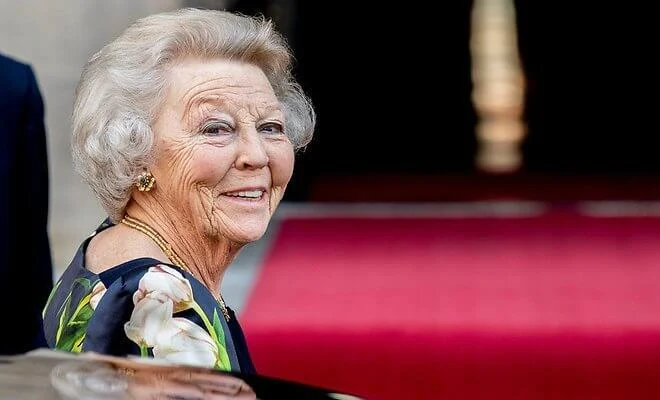 Princess Beatrix of the Netherlands wore a navy blue floral tulip print blouse, and navy blue trousers. Gold necklace