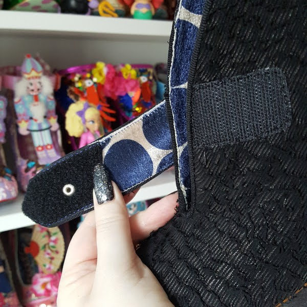holding open strap of shoe in hand showing Velcro fastening closure and polka dot velvet lining