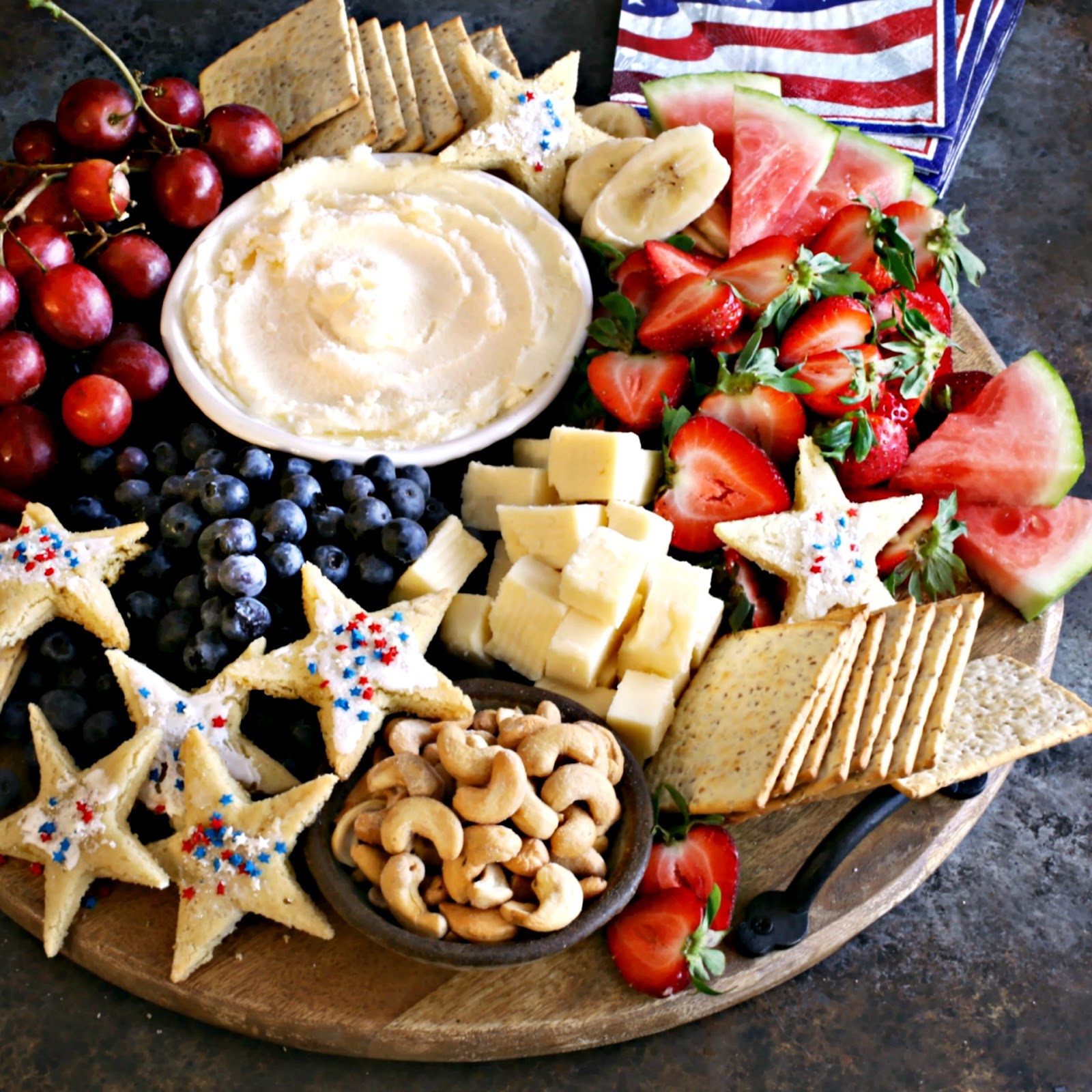 Patriotic themed charcuterie board with red, white and blue fruit and star shaped cookies.