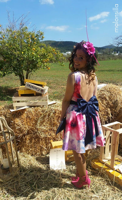 Invitada a boda perfecta con vestido estampado corto, bolso abanico azul navy, zapatos tacón lace up fucsia y tocado tipo casquete con orquideas, lazo grande en la espalda