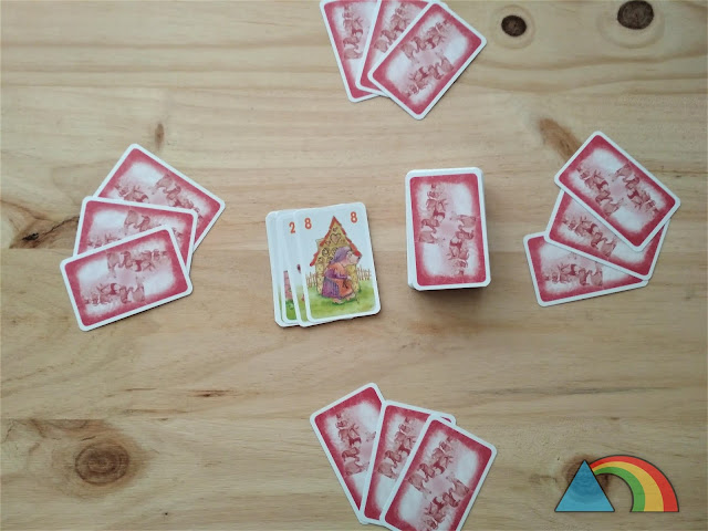 Preparación del juego Los 10 cerditos: Mazo de cartas en el centro de la mesa, y tres cartas repartidas para 4 jugadores