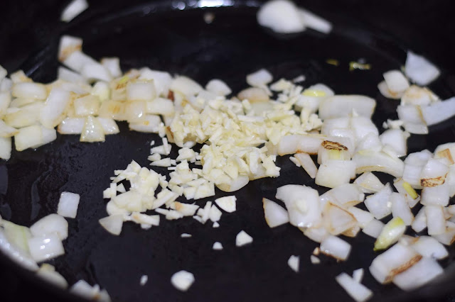 Minced garlic being added to the cast iron skillet with the onion. 