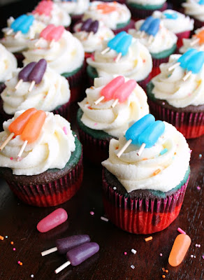 Fun multicolored cupcakes that are made from a doctored up cake mix and topped with a simple but cute popsicle decoration. These cupcakes will have you singing sweet summertime! sweet summertime cupcakes with extra spinkles and mike and ikes in front