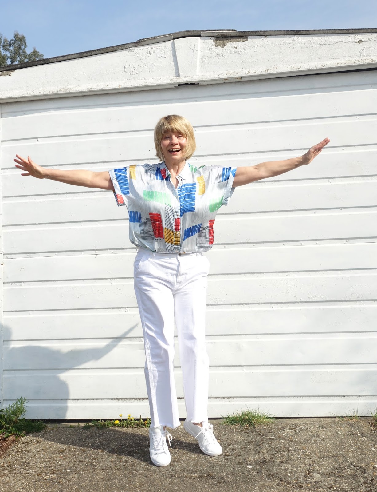 Jump[ing for joy: mid life woman in white wide legs jeans and geometric print blouse