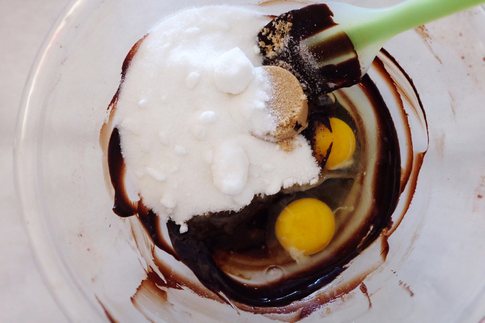 adding sugar and eggs to butter and cocoa powder