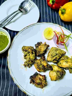 Serving hariyali kabab in a garnished plate green chutney, bell pepper and tablespoon in background