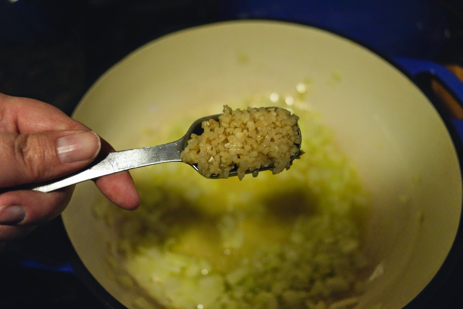 The minced garlic being added to the pot with a metal measuring spoon.