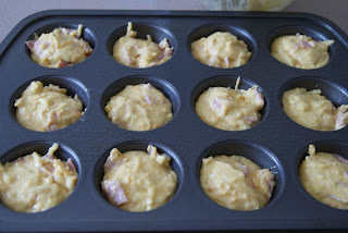 Corn brad mix with ham and shredded cheese evenly distributed in a muffin baking pan ready to be cooked in the oven.