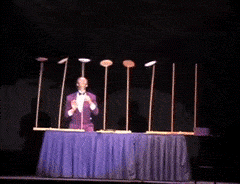 Gif of person spinning 6 different plates at the top of wooden poles.