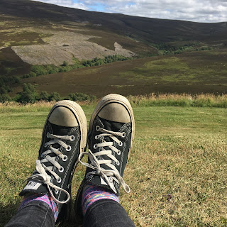 Shoes and part of leg in foreground with green countryside hills in the background