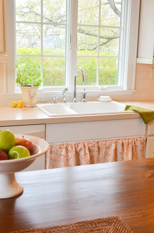 Cottage style kitchen sink area with red and white sink skirt and plants.