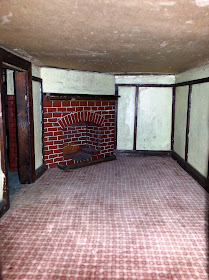 Inside view of a 1930s vintage dolls' house bungalow showing a red brick corner fireplace and dark wooden beading.