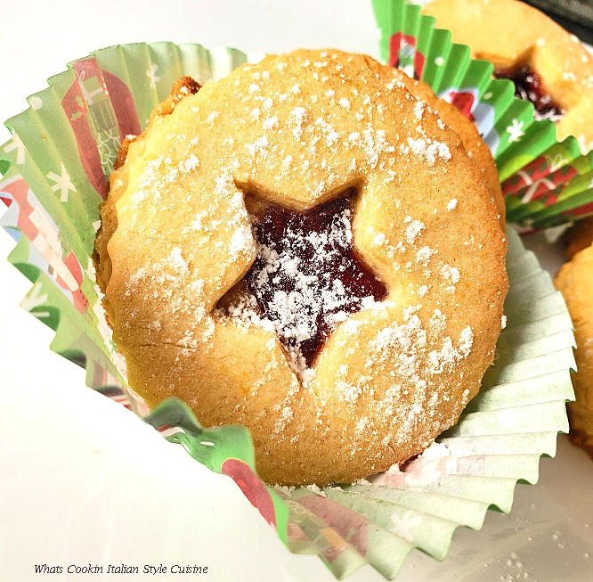Italian Raspberry Jam Filled Cookies this is a linzer cookie filled with raspberry jam in a christmas paper liner with Santa on it