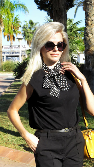 Alejandra Colomera con camiseta negra, pantalón formal negro, lazo en el cuello negro con lunares blancos y complementos mostaza