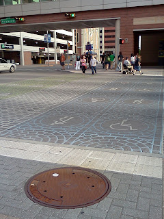 Crosswalk in downtown Indianapolis with blue painted lane with wheelchair user symbol. To the left is a walking lane & a bike lane to the convention center