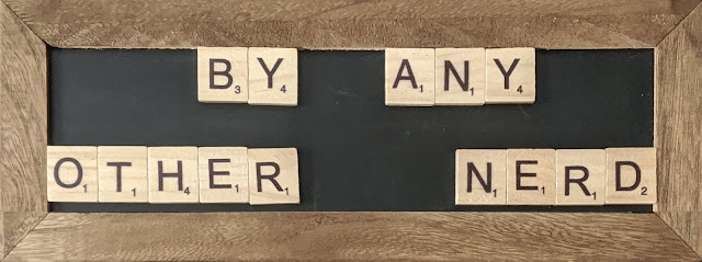 A chalkboard with scrabble letters that spell out "By Any Other Nerd"