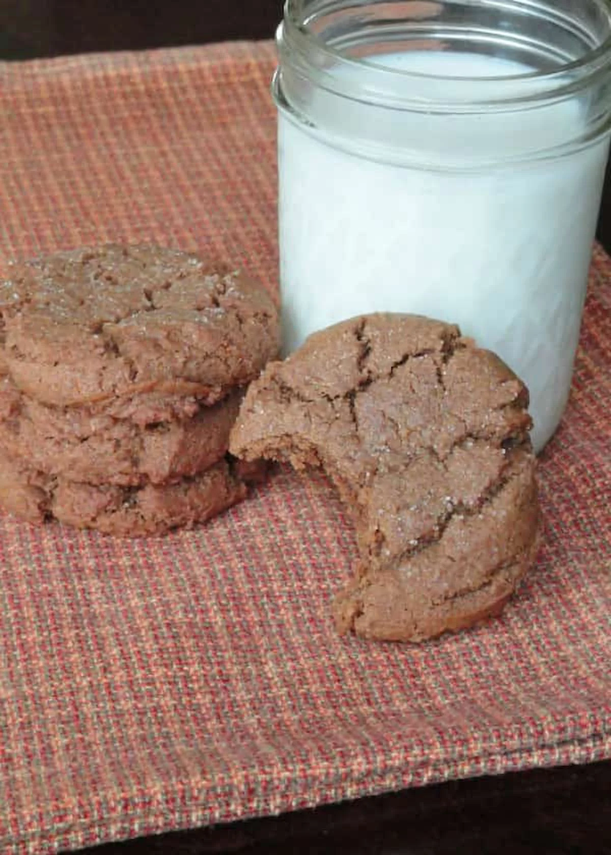 Molasses Cookies stacked on an orange kitchen towel with one Molasses Cookie resting on its side with a bite missing.