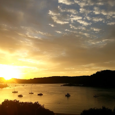 View across an inlet at sunrise, with the sun just coming up behind a hill.