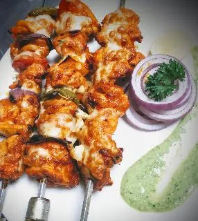 Chicken cheese kebab Shewer on a serving plate with green chutney and onion slices