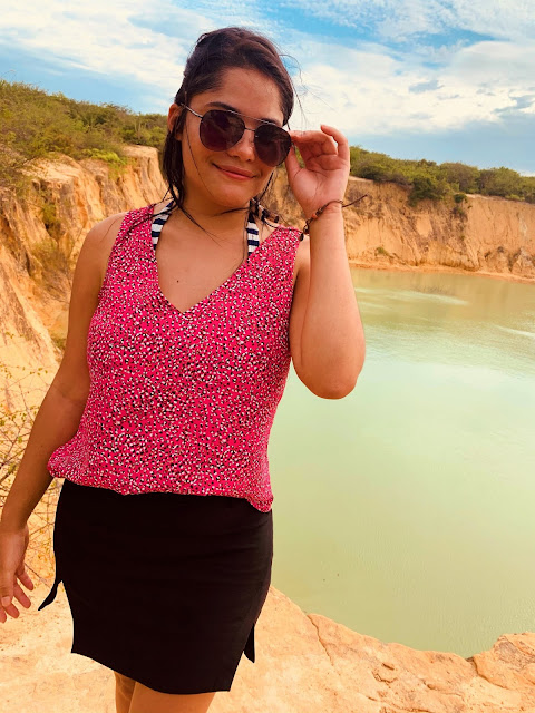 Passeio Quadriciclo em Parnaíba mulher morena, jovem, cabelo preto, oculos escuros, blusa rosa e saia preta com a paisagem de uma lagoa verde ao fundo