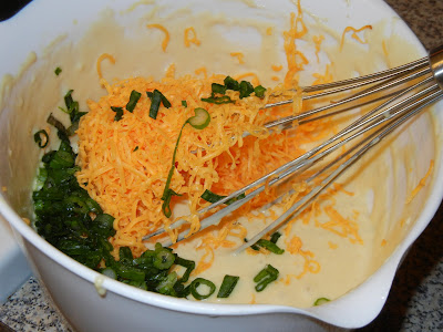 bowl with waffle batter, green onions, and shredded cheese and a metal whisk 