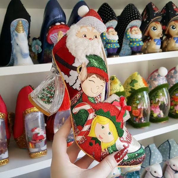 Santa and elf character shoe held in hand in shoe room with shelves of shoes behind