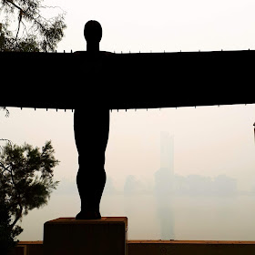 Maquette of the Angel of the North sculpture against a smokey Lake Burley Griffin.