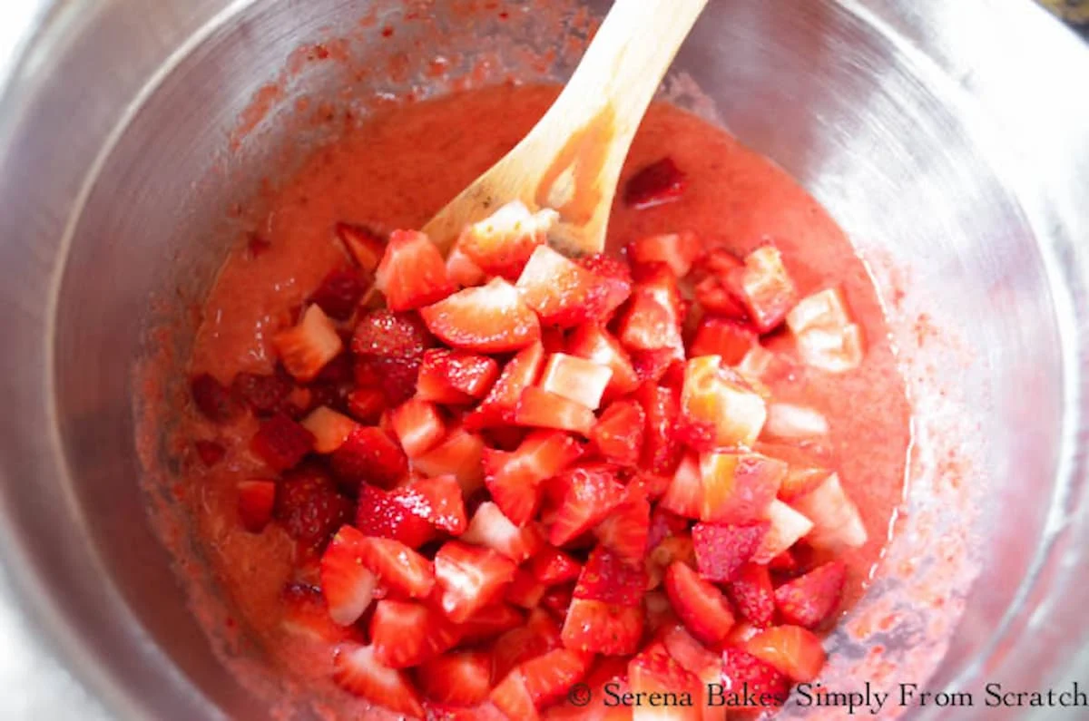 Diced strawberries and strawberry puree being mixed together in a stainless steel mixing bowl.