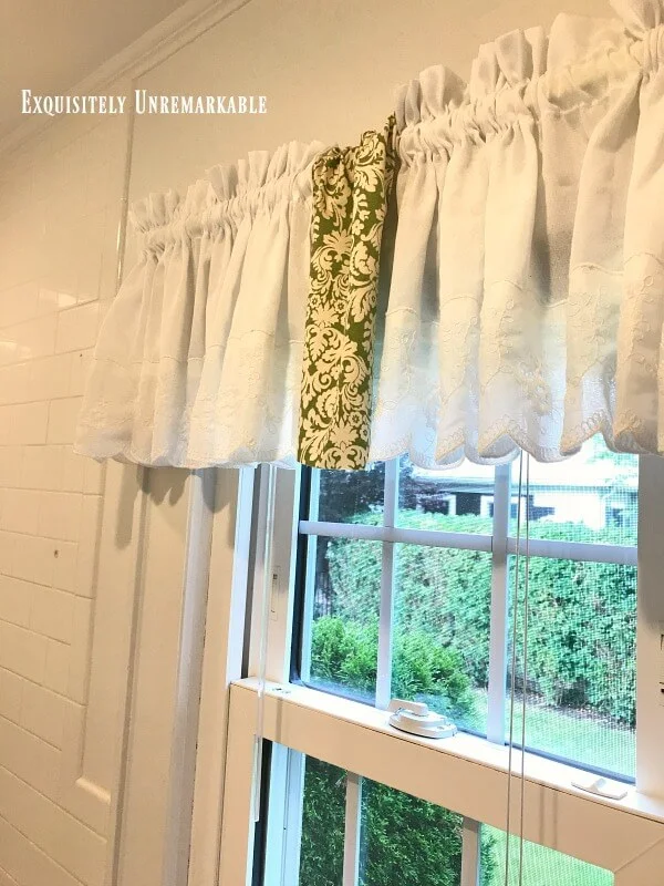 White curtain with a strip of green fabric hanging in middle on bathroom window