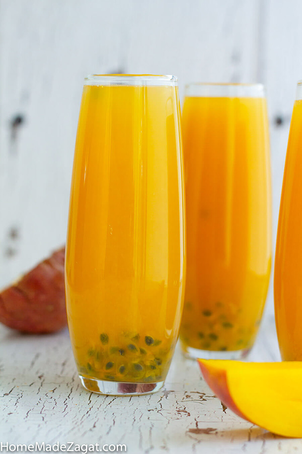Three completed glasses of mango passion fruit juice with passion fruit seeds as a garnish.
