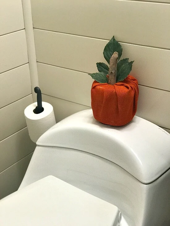 Bathroom with orange burlap toilet paper cover on toilet.