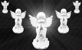 Five figurines of angels with praying hands and rays of light behind on black background