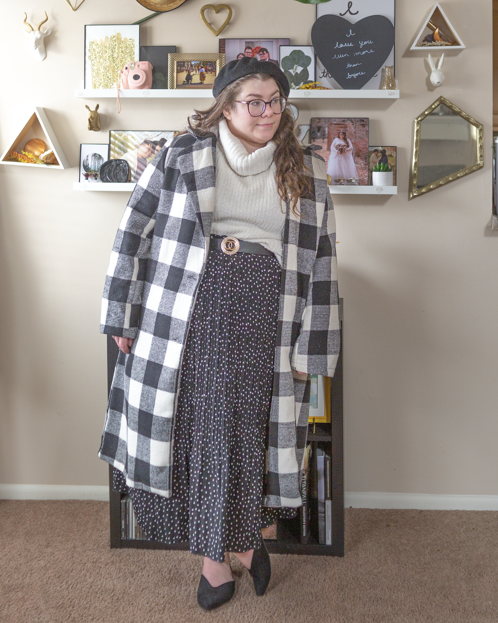 An outfit consisting of a black beret, a black and white gingham single breasted long coat over a white chenille turtleneck half tucked into a black pleated swiss dotted maxi skirt and black slingback pointed toe flats.