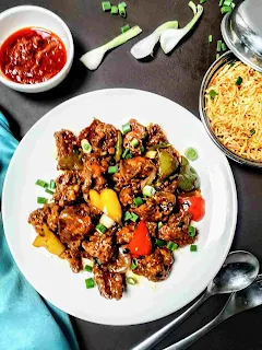 Chilli chicken serving with fried rice, Schezwan sauce, spoon and fork in background