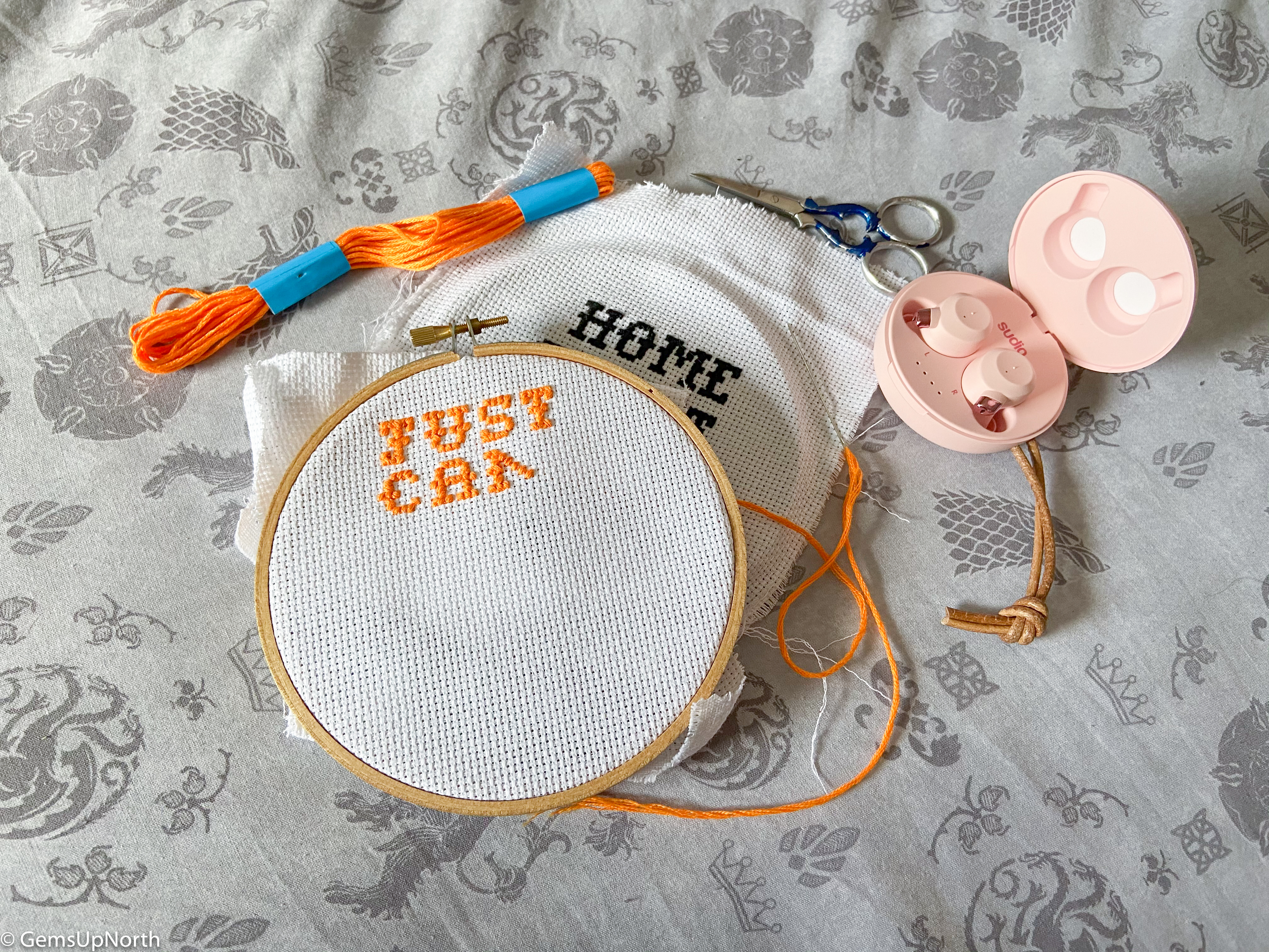 Flat lay of FEM Sudio Ear Buds with Cross stitch project.