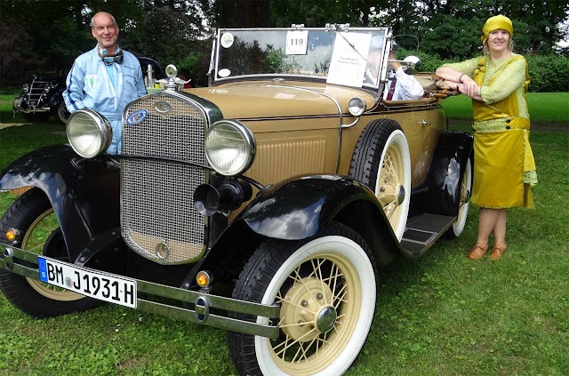 Historischer Ford gruppiert von Dame in stilechtem Charleston grünenKleid und Mann mit Mechaniker Uniform. Historischer Ford mit Mann in Mechaniker Uniform und Dame mit grünem Charleston Kleid
