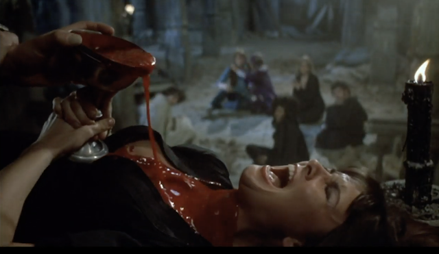 A woman in a low-cut dress lying down, screaming as blood pours from a chalice balanced on her chest