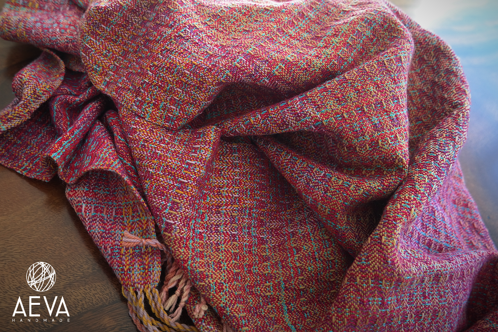 A close-up shot of the mostly pink wrap, with pops of turquoise, yellow, and purple, which is scrunched up on a wooden table