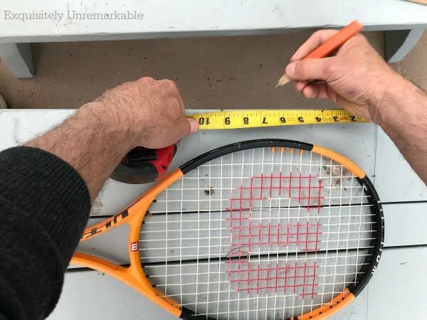 Measuring and marking a wooden bench with a pencil and a tennis racket