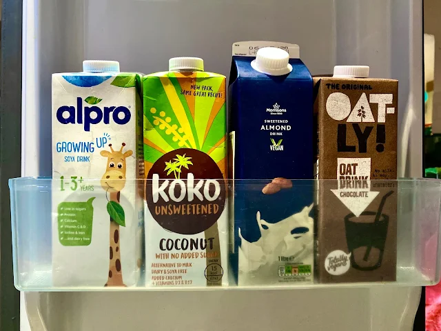 A fridge shelf with: alpro growing up soya drink, Koko unsweetened, Almond drink and oatly chocolate milks