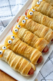 Crescent rolls wrapped around hot dogs to look like mummies on a white platter with eyes