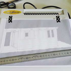 Lightbox with a sketch of a holiday house and a sheet of tracing paper on top.
