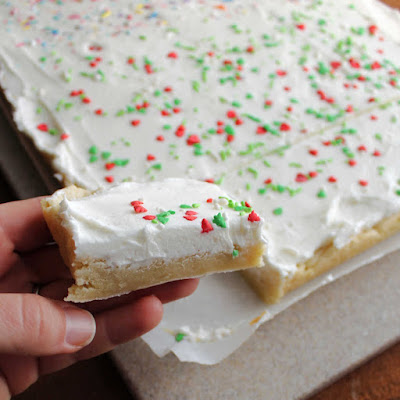 Super soft sugar cookie bars topped with a fluffy layer buttercream are a fun and easy treat. They are so much quicker to make than individual cookies and taste great! hand holding piece of soft sugar cookie bar with white buttercream