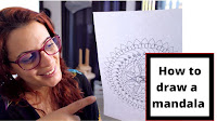In this picture there is a mandala artist holding a mandala drawing in her hand
