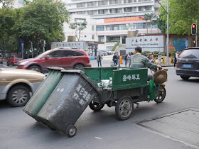 "City Cleaning" pulling two garbage bins with a three-wheeled motorized vehicle